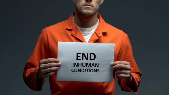 End-inhuman-conditions-phrase-on-card-in-hands-of-Caucasian-prisoner,-protest