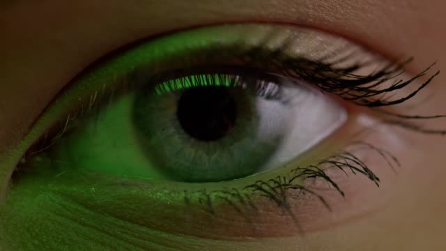 Close-up-shoot-of-light-blue-eye-blinking-with-reflection-of-lamp-on-it-in-green-light.