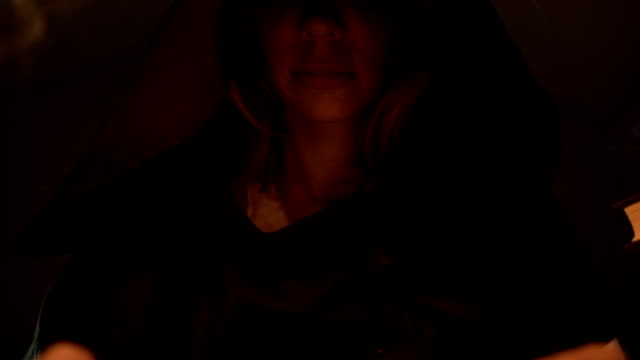 Close-up-girl-magician-in-the-hood-in-a-dark-room-by-candlelight-reads-a-spell.-Low-key-live-camera.-Mystic.