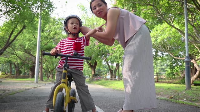 Mother-helping-her-son-(Long-hair-boy)--to-put-on-bicycle-helmet-outdoors.