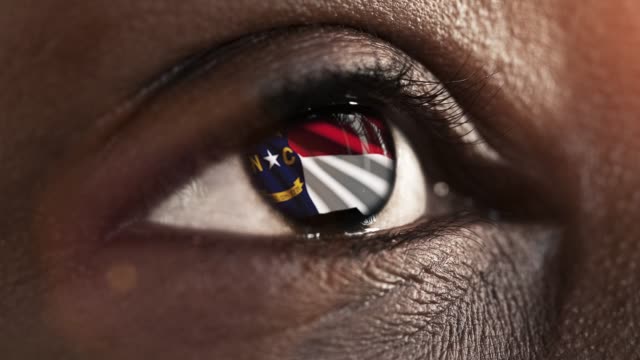 Mujer-ojo-negro-en-primer-plano-con-la-bandera-del-estado-de-Carolina-del-Norte-en-iris,-estados-unidos-de-América-con-movimiento-de-viento.-concepto-de-vídeo