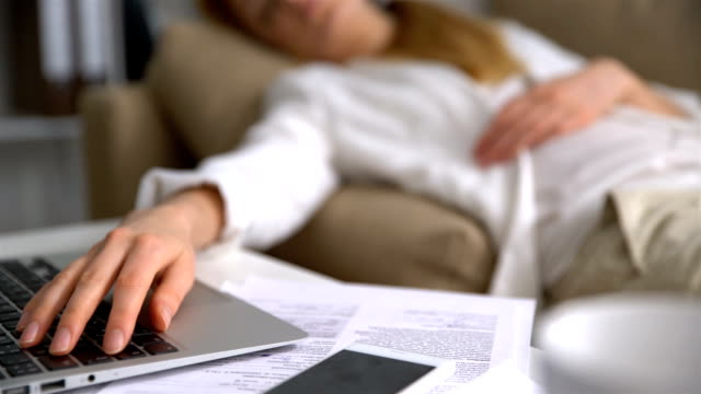 Müde-junge-Geschäftsfrau-schlafend-auf-der-Couch-im-Büro-mit-Laptop-Nahaufnahme-ihrer-Hand-auf-der-Tastatur