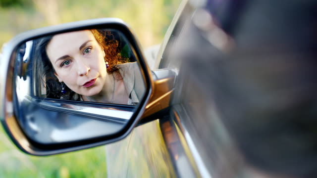 A-woman-with-a-weeping-is-sitting-in-the-car.-In-the-rear-view-mirror-corrects-make-up,-all-in-tears.-Concept---depression,-problems