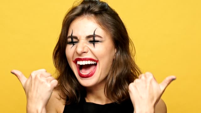 Happy-cheerful-lady-with-dark-make-up-and-right-red-lipstick-smiling-amd-showing-thumbs-up-isolated-over-yellow-background