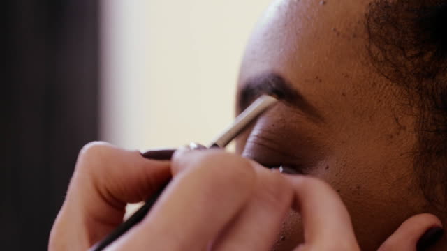 Face-makeup-artist-during-painting-eyebrows-on-woman-face-in-beauty-studio