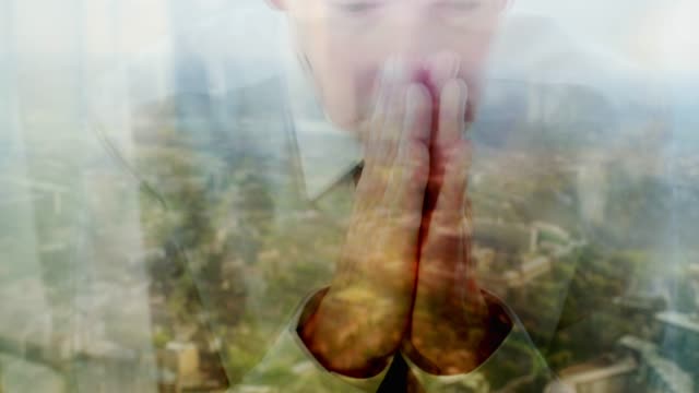 Reflection-of-a-businessman-praying-against-a-window