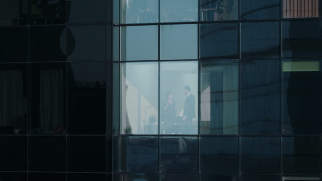 Luftaufnahmen-von-außen:-Geschäftsmann-und-geschäftsfrau-sprechen-Unternehmen-stehen-neben-Wolkenkratzer-Bürofenster.-Schuss-des-finanziellen-Geschäftsviertels-der-Stadt-fliegen.