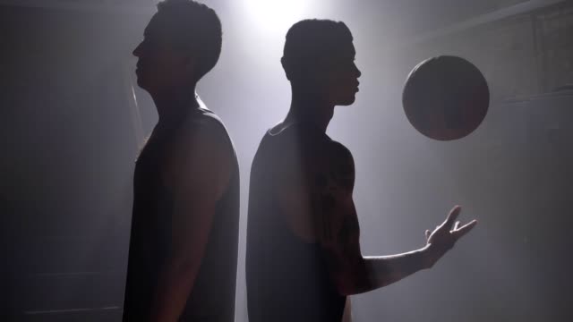 Zwei-Basketball-Spieler-Schatten-stehen-Rücken-an-Rücken-in-nebligen-Zimmer-mit-Flutlicht