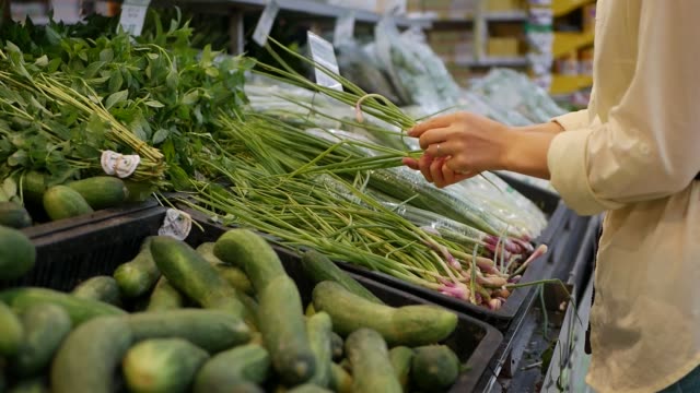 Female-hands-chooses-onion-leaf-in-the-supermarket.-Young-woman-buying-healthy-food-in-the-blur-background-of-a-store