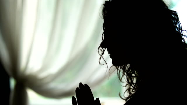 Weibliche-in-Silhouette-Bögen-im-Gespräch-mit-Gott-im-Gebet-gefalteten-Händen,-drinnen