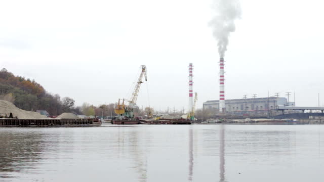 The-industrial-port-pour-sand-on-the-barge-with-a-crane.-In-the-background---thermal-power-plant