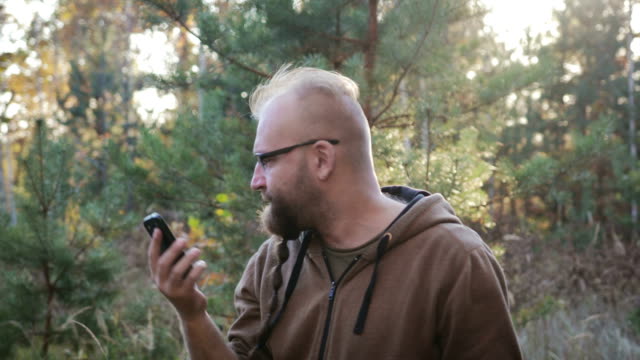 Ein-junger-Mann-mit-einem-Bart-schwört-und-schreit-auf-dem-Handy-gegen-den-herbstlichen-Wald