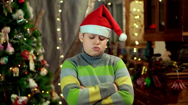 El-niño-con-el-suéter-y-sombrero-de-Santa-Claus-es-molesto-y-ofendido.-No-tiene-ningún-regalo.-contra-el-fondo-de-luces-de-Navidad