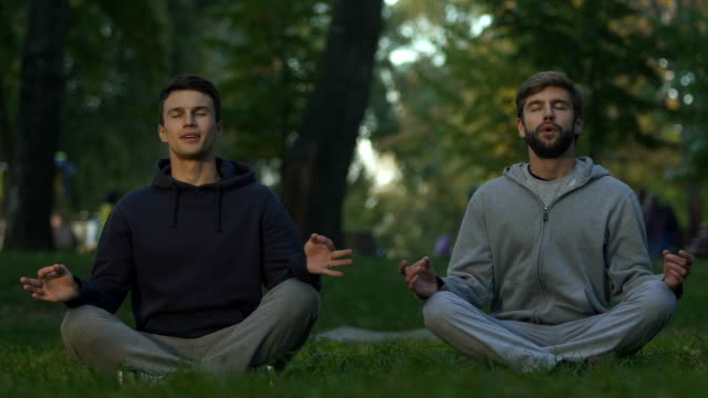 Male-friends-sitting-in-lotus-position,-practicing-yoga-in-city-park,-meditation