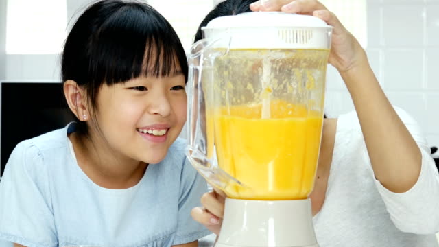 Mutter-und-mit-wenig-Saft-Mixer-in-der-Küche.-Sie-machen-Orangensaft-trinken.-Menschen-mit-Lebensstil-und-gesunde-Konzept.