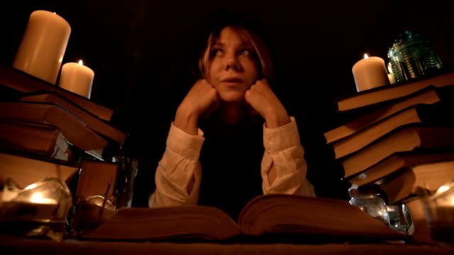 Nahaufnahme-eines-gelangweilten-Mädchenzauberers-in-einem-dunklen-Raum-bei-Kerzenschein-tummelt-sich-in-einem-Buch-und-meditiert.