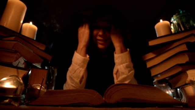 Close-up-of-a-bored-girl-magician-in-a-dark-room-in-candlelight-dabbles-in-a-book-and-meditates.