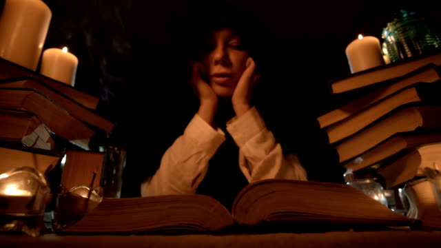 Primer-plano-de-una-niña-maga-aburrida-en-una-habitación-oscura-en-la-luz-de-las-velas-incursiona-en-un-libro-y-medita.