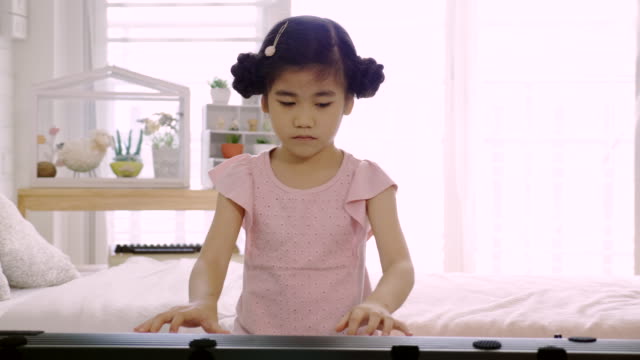4K:-Chica-asiática-está-entrenando-para-tocar-un-piano-eléctrico.-Es-una-actividad-que-entrena-las-habilidades-emocionales-y-el-cuerpo-bien-estudiar-en-casa-o-escuela-de-música-Música.-buena-salud-mental-y-buen-humor.
