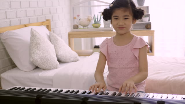 4K:-Asiatische-Skid-Mädchen-trainiert,-um-ein-E-Piano-zu-spielen.-Ist-eine-Aktivität,-die-emotionale-Fähigkeiten-trainiert-Und-der-Körper-gut-studieren-zu-Hause-oder-Musikschule-Musik.-gute-psychische-Gesundheit-und-gute-Laune.