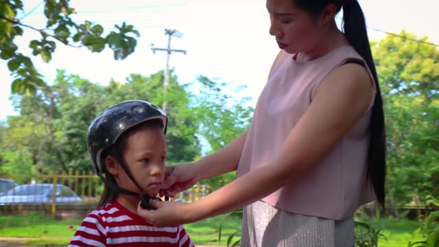 Madre-ayudando-a-su-hijo-(niño-de-pelo-largo)-a-ponerse-el-casco-de-la-bicicleta-al-aire-libre.