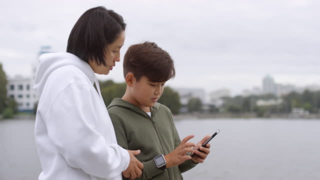 Madre-asiática-e-hijo-usando-Smartphone-antes-del-entrenamiento-al-aire-libre