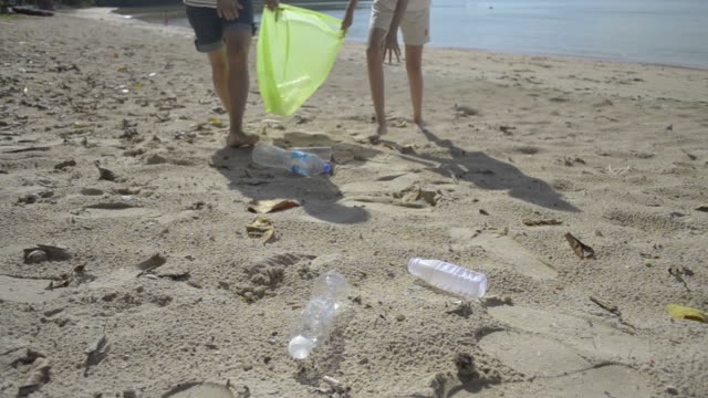 Mama-und-ihre-Tochter-sammeln-Müll-am-Sandstrand-in-grüne-Plastiktüte,-Plastikflaschen-werden-am-Strand-gesammelt,-Freiwillige-reinigen-den-Strand.
