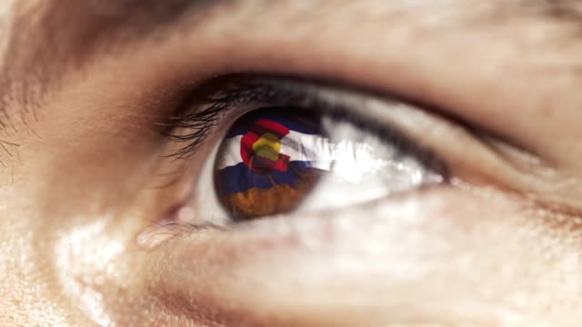Mann-mit-braunem-Auge-aus-nächster-Nähe,-die-Flagge-des-Colorado-Staates-in-Iris,-vereinigte-Staaten-von-Amerika-mit-Windbewegung.-Videokonzept