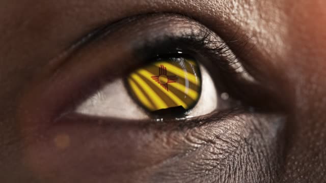 Woman-black-eye-in-close-up-with-the-flag-of-New-Mexico-state-in-iris,-united-states-of-america-with-wind-motion.-video-concept