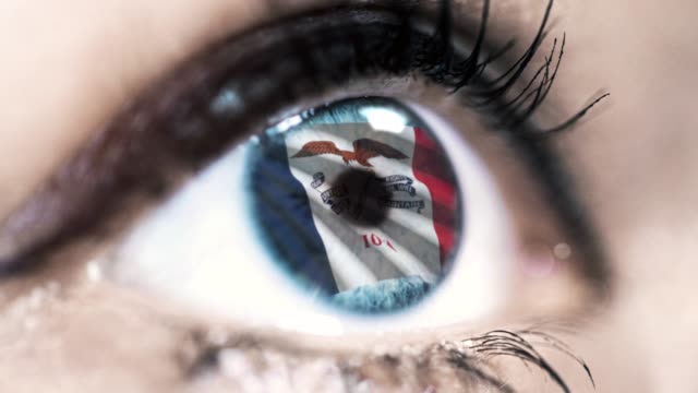 Woman-blue-eye-in-close-up-with-the-flag-of-Iowa-state-in-iris,-united-states-of-america-with-wind-motion.-video-concept