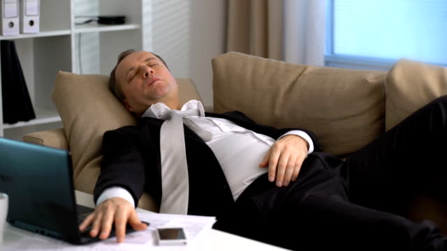 Müde-Geschäftsmann-schläft-auf-dem-Sofa-im-Büro