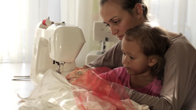 Young-attractive-mother-working-on-sewing-machine-with-her-little-cute-daughter