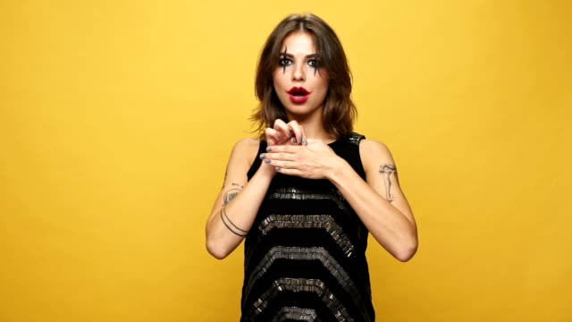Young-strange-woman-with-creepy-make-up-showing-focus-with-finger-and-laughing-isolated-over-yellow-background