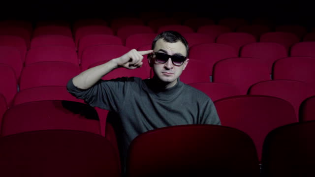 Single-man-sitting-in-comfortable-red-chairs-in-dark-cinema-theater-and-twists-her-finger-at-her-temple