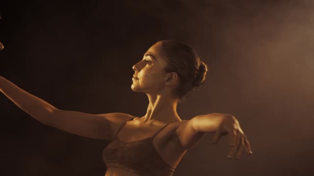Close-up-portrait-of-beautiful-young-ballet-dancer-with-shining-golden-skin-on-black-background.-Body-art-with-gold-paint.-Ballerina-in-tutu-dancing-on-smoke-stage.-Slow-motion
