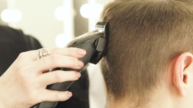 Frau-Friseur-männliche-Haare-schneiden-mit-elektrischen-Rasierapparat-im-Beauty-Studio.-Männliche-Frisur-mit-Haarschneider-im-Barbershop-hautnah.-Frau-Hairdcutter-arbeitet-mit-Kunden