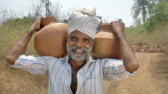 Glücklich-und-lächelnd-männlichen-Bauer-tragen-zwei-Irdene-Töpfe-gefüllt-mit-Süßwasser-auf-seiner-Schulter