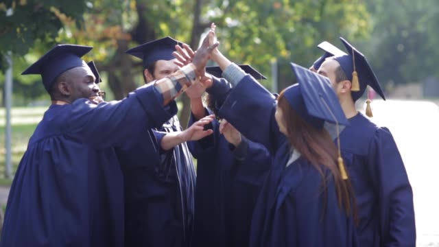 happy-students-in-mortar-boards-making-high-five