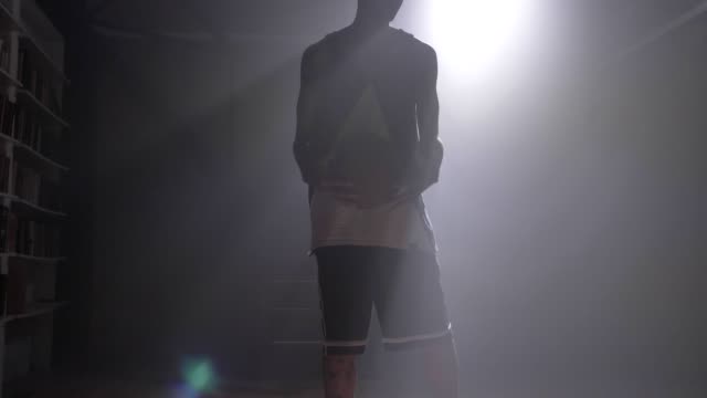 Jugador-de-uno-baloncesto-jugando-con-bola-en-habitación-oscura-niebla-con-proyector