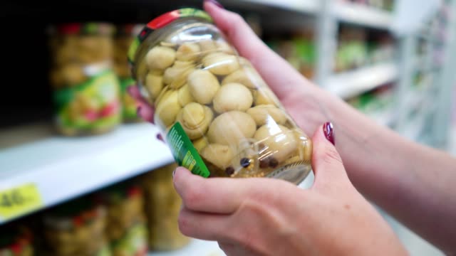Closeup-caucasian-woman-hands-near-shop-shelves-choosing-marinade-mushrooms-in-grocery-market