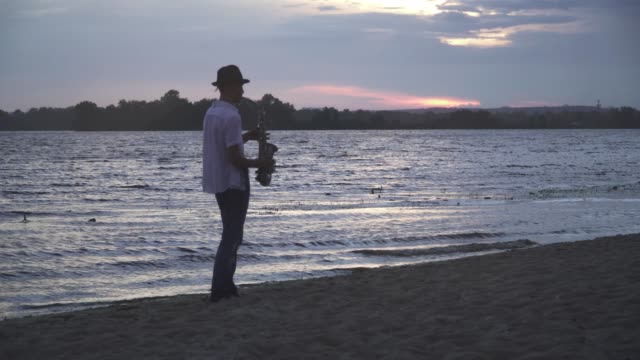 Hübscher-junger-Kerl-spielt-Saxophon-am-Ufer-Flusses