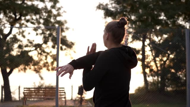 Caucasian-young-woman-warming-up-in-morning-on-basketball-court.-Stretching-her-arms-before-basketball-training.-Backside-footage