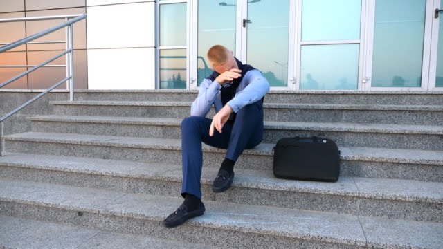 Dolly-shot-of-desperate-young-businessman-sitting-on-stairs-near-office-building-and-taking-off-cardigan-of-the-shoulders-with-anger-outdoor.-Upset-sad-manager-got-a-very-bad-news-and-crying.-Close-up