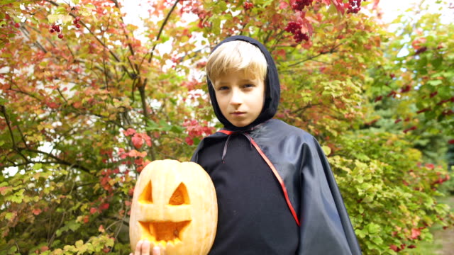 Boy-in-Halloween-costume-holding-pumpkin-jack-o-lantern,-alone-in-forest,-spooky