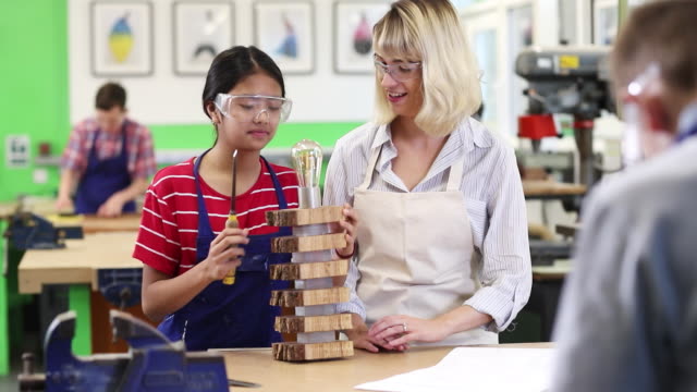 Profesor-ayuda-mujer-alta-escuela-estudiante-edificio-lámpara-en-lección-de-carpintería