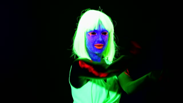 Woman-with-UV-face-paint,-wig,-glowing-clothing-dancing-in-front-of-camera,-shoulder-shot.-Caucasian-woman.-.