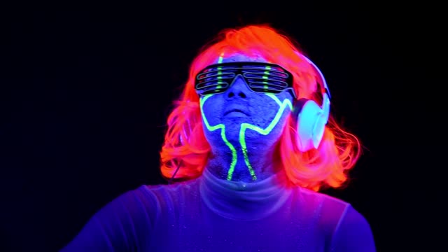 Slow-motin-of-Woman-with-UV-cyborg-face-paint,-wig,-glowing-glasses,-clothing-dancing-and-listening-to-music-with-headphones.-Asian-woman.-.