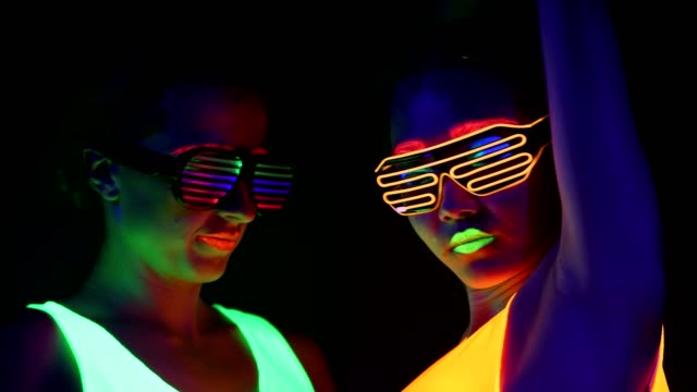 Women-with-UV-face-paint,-glowing-clothing,-glowing-bracelet,-glasses-dancing-in-front-of-camera,-face-shot.-Caucasian-and-woman.-.