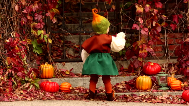 A-little-girl-in-a-medieval-gnome-costume-touches-the-leaves-of-a-red-vine-plant