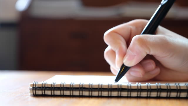 die-Hand-einer-Frau-schreiben-auf-leere-Notebooks-auf-Holztisch